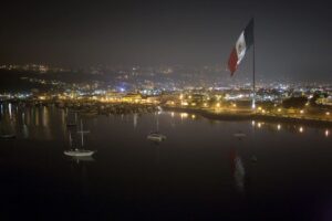 Fotografía del puerto de Ensenada iluminado, con la bandera monumental al fondo