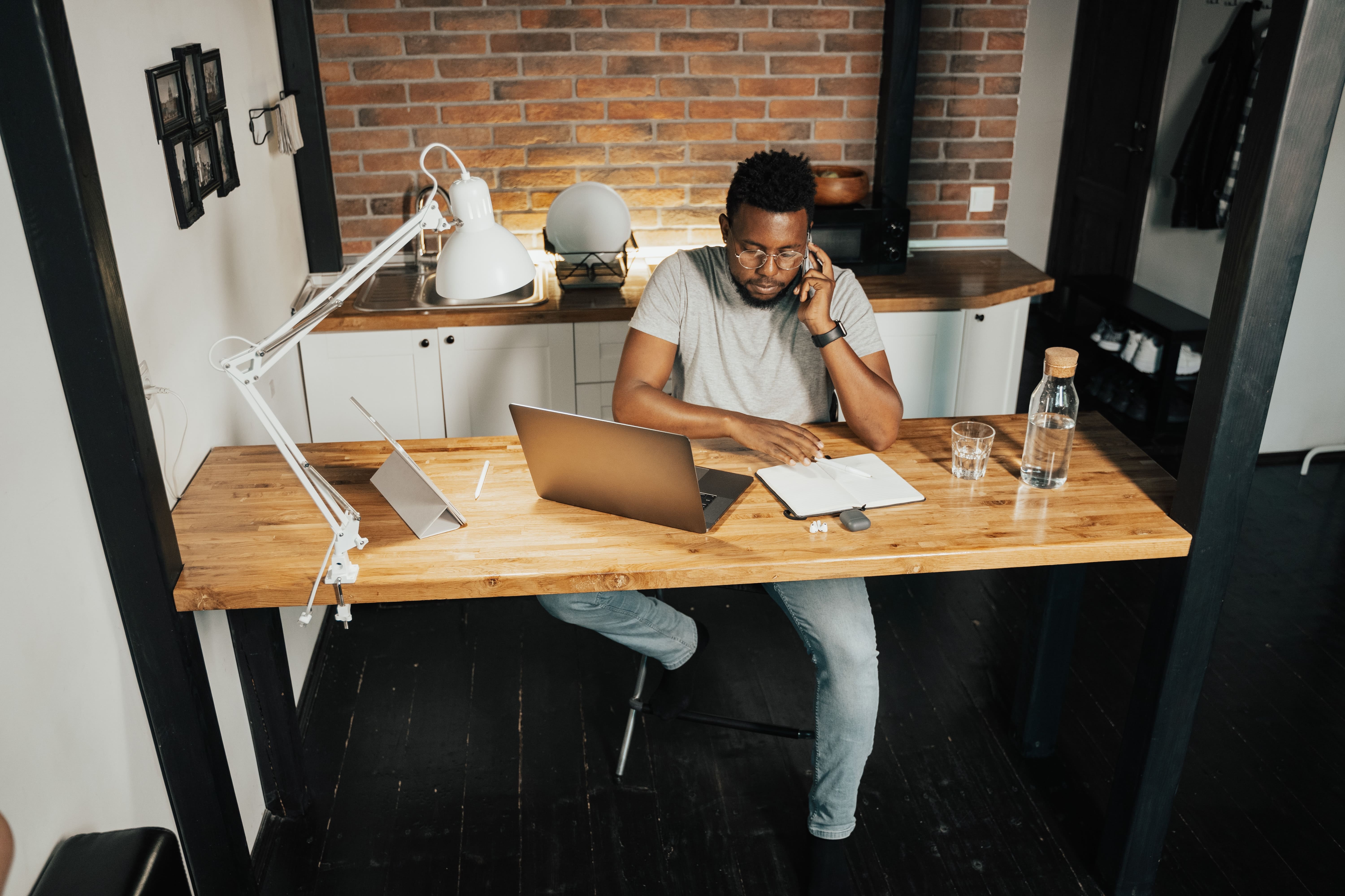 Fotografía de un hombre trabajando en su escritorio, hablando por teléfono y usando su laptop