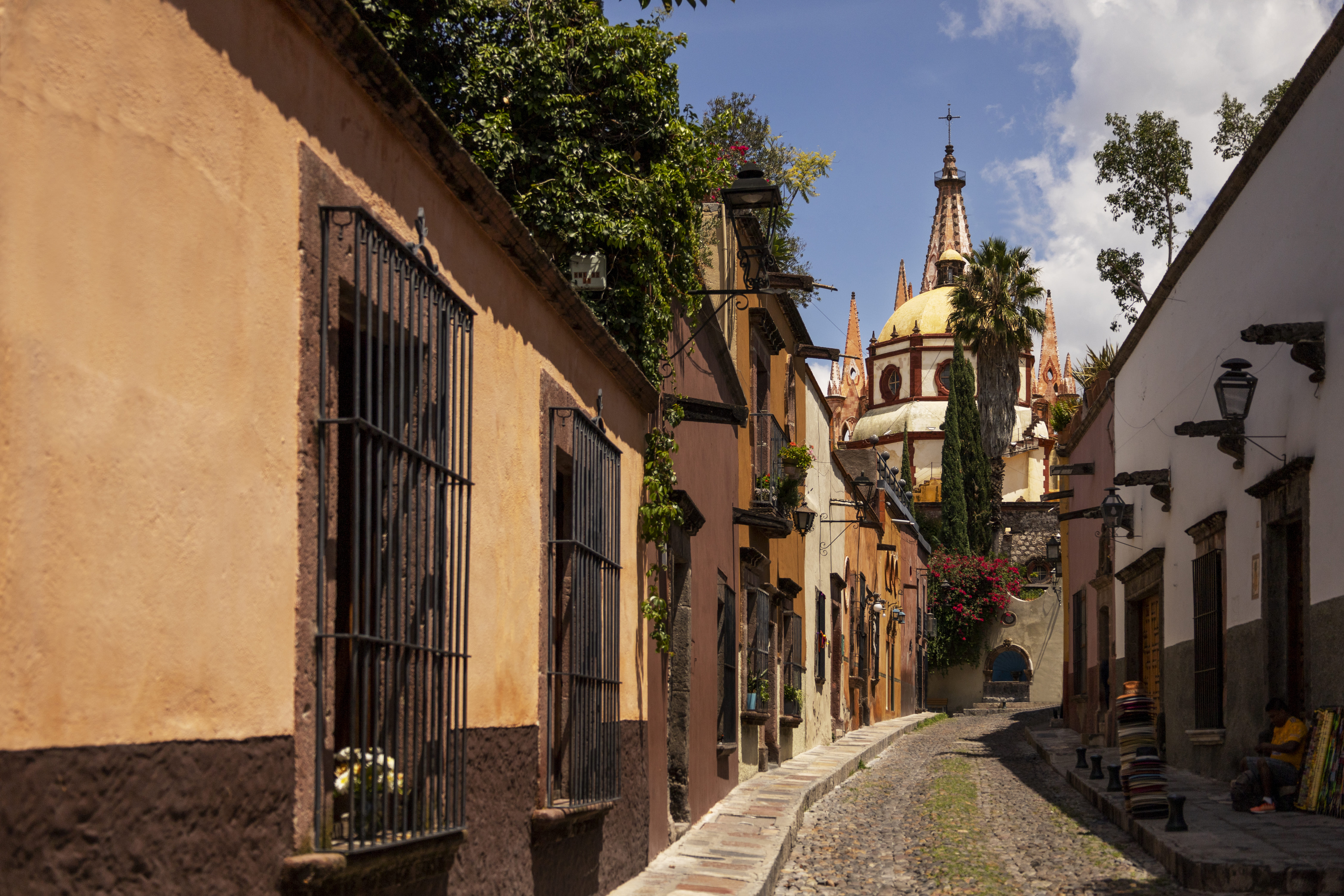 Vista de una de las bellas calles empedradas en Cholula, con inmuebles a ambos lados y de fondo una icónica iglesia de la ciudad. Un lugar pintoresco, ideal para rentar tu departamento en Cholula.