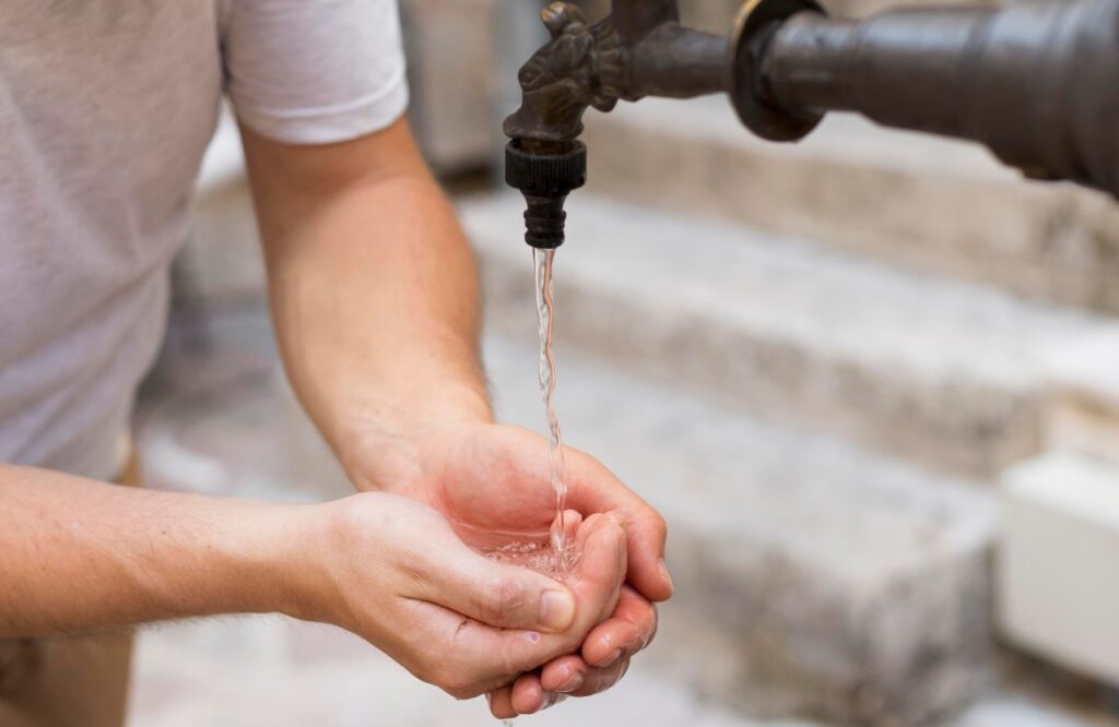 Hombre que enfrenta desabasto de agua potable en su edificio lavándose las manos en el exterior.